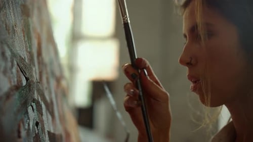 Young woman painter taking paintbrush for work in her bright art studio