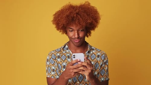 Smiling guy using smartphone isolated on yellow background in studio