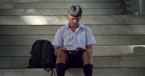 A male high school student in a white school uniform is sitting and studying alone