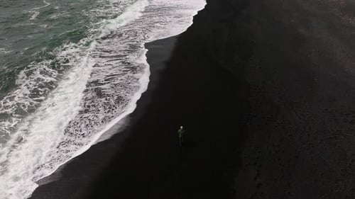 Man Walking Along Tide on Black Sand Beach