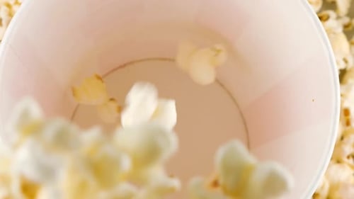 Popcorn grains falling into red and white striped bucket on background popcorn grains.