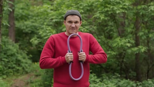 Um esportista profissional com uma camisa vermelha é visto segurando um expansor de anel roxo para Pilates enquanto