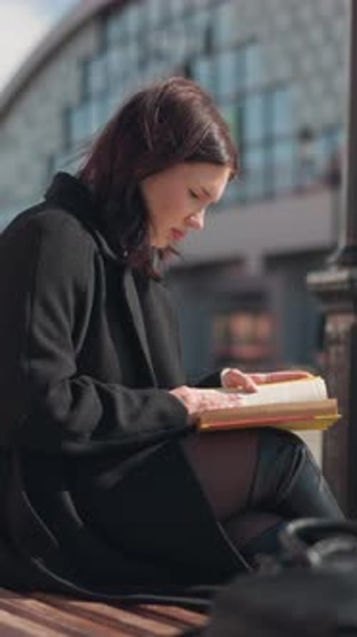 Back View of Woman Reading Book Outdoors in Urban Setting