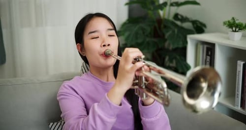 Young Woman Playing a Trumpet on Couch at Home