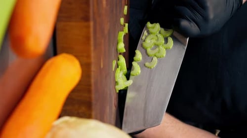 Vertical Video Closeup in a Professional Kitchen Wearing Black Gloves Cuts Celery on Wooden Board