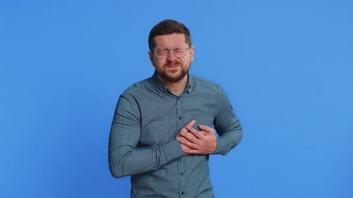 Man Clutches Chest in Discomfort on Blue Background