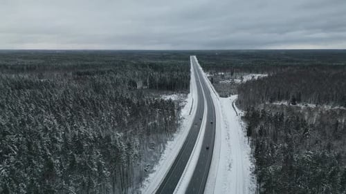 Stunning Aerial Footage Capturing a Snow Covered Highway Gently Lined with Beautiful Tall Forests