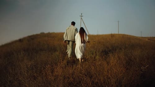 Young couple walking up the hill. Love concept. Free spirit in nature. Beautiful field on the hills