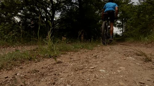 Shot from below of a cyclist slowly cycling on a dirt road on a sunny summer day. Sportive outdoor a