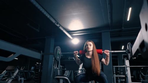 portrait of a concentrated fitness woman doing a heavy shoulder press exercise with a barbell in gym