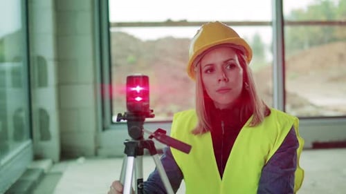 Junge Ingenieurin steht mit Laserwaage auf einer Baustelle