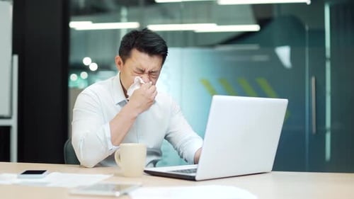 Man Sneezes While Working on Laptop in Office