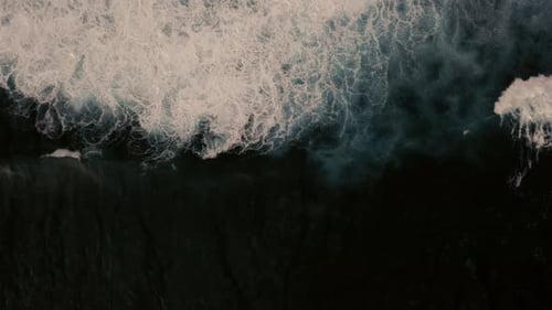 Aerial birds eye view of dramatic dark moody ocean water with white foaming waves breaking