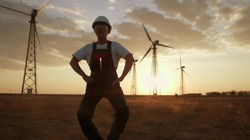 Cheerful electrical engineer is having fun dancing against backdrop of wind turbine towers in field