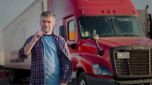 Professional Truck Driver Approaches His Truck and Behind Him Parked Long Haul SemiTruck Close Up