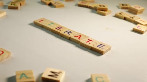 Le mot Iterate orthographié avec des lettres en carreaux de bois. Fond blanc cassé. Lumière Théâtral. Avion plat