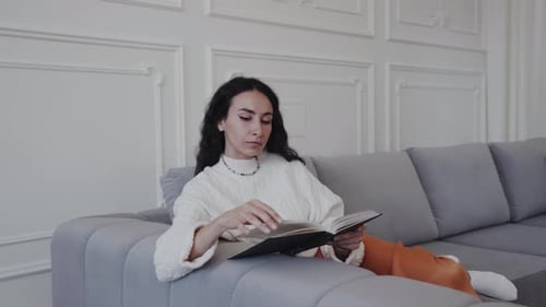 Eine Frau sitzt bequem auf der Couch und liest ein Buch in ihrem Haus