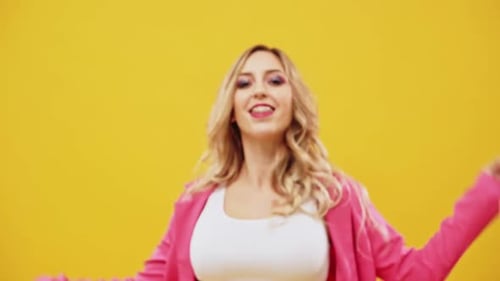 Woman Dancing in Pink Blazer on Yellow Backdrop