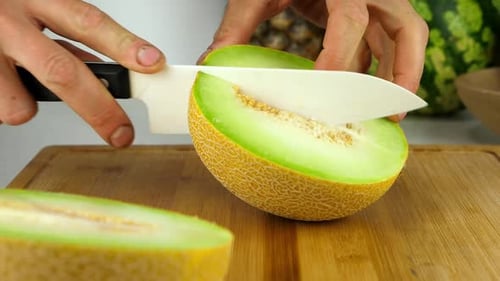 Melone auf einem Bambus-Schneidebrett mit einem Keramikmesser schneiden