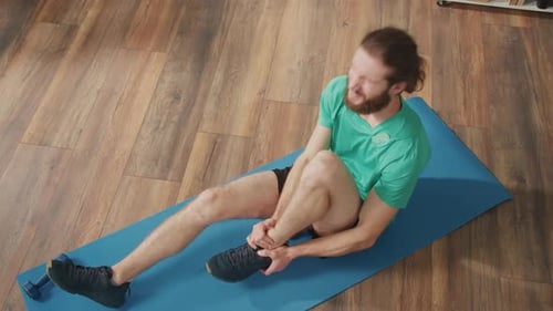 Young Man Sits on the Floor at Home Got Injured in Training Holding on the Ankle