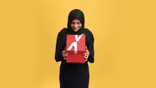 Overjoyed Muslim Woman Open Festive Red Gift Box with Desired Present Posing Isolated on Orange