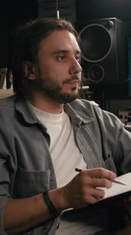 Vertical of Young Male Podcast Host Writing Interview Questions in Studio