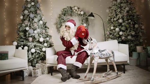 Santa Claus Holding Present on Couch at Home