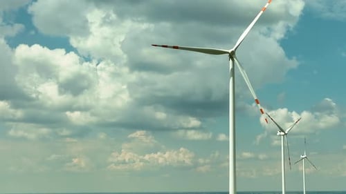 Aerial footage featuring a row of wind turbines set against a sky filled with dynamic, fluffy clouds