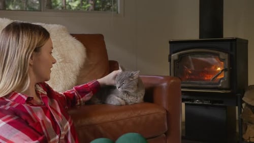 Woman Pets Cat by Cozy Fireplace at Home