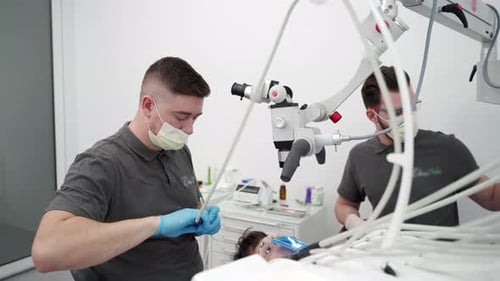 Odontólogo masculino que trata endodoncias con microscopio en una clínica de estomatología moderna, asistente dental