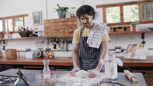 Caucasian man preparing bread dough using tablet in kitchen, slow motion