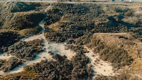 Aerial birdseye above sandy dune terrain tilt up to coastal ocean road horizon