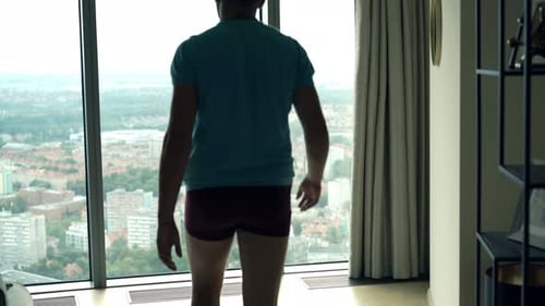 Man Stands in Apartment Overlooking City