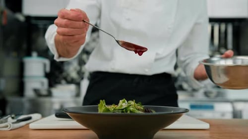 Professional kitchen the chef pours red sauce on the salad with pear and cheese mixes the ingredient