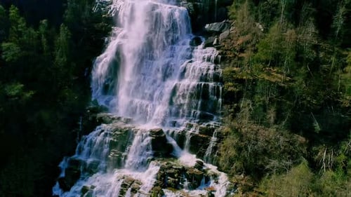 Close-up slowmotion drone lifting shot of water falling down from a high waterfall