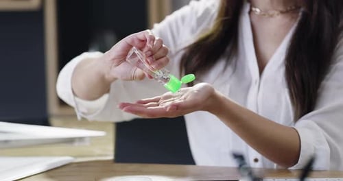 4k video footage of a businesswoman disinfecting her hands before using a laptop in a modern office