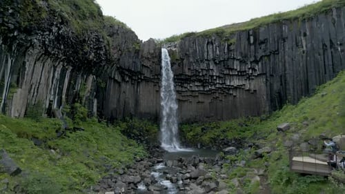 Svartifoss Waterfall Flowing Down To The River At Daylight In Iceland. - aerial approach