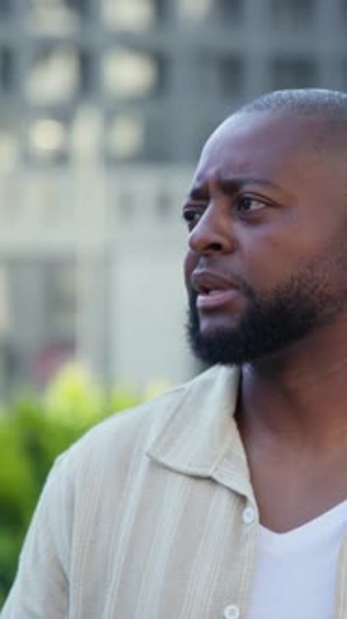 Vertical video: Tracking off camera blur, African man wearing beige shirt on rooftop, responding