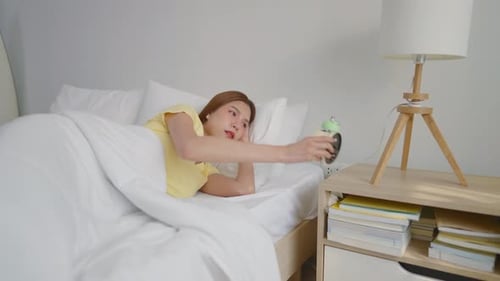 Asian attractive young woman turn off alarm clock ringing in the morning.