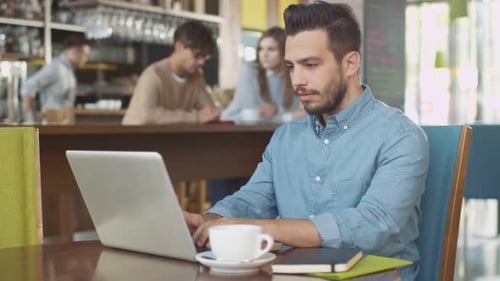 Hispanic Ethnicity Young Man using Laptop Computer at Cozy Coffee Shop.