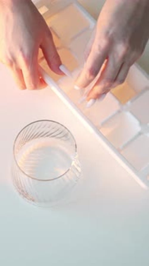 Hands Adding Ice to a Glass of Water