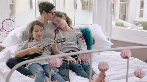 Children with adult play ukulele on bed