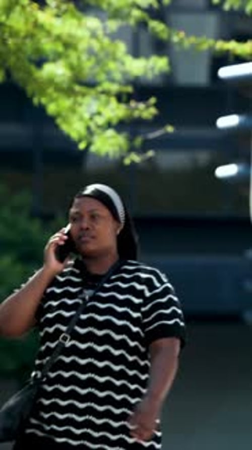 Vertical video: Entering woman in striped shirt, white headband walking street, taking phone call