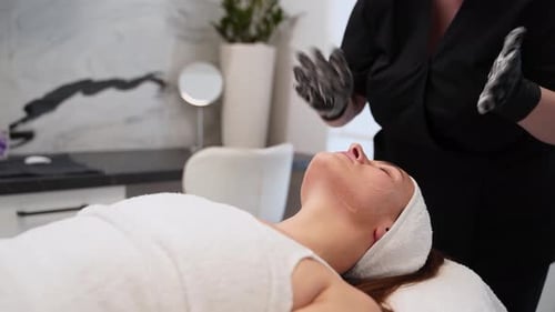 Professional Beautician Applies Facial Mask for Skincare Treatment on Woman at Modern Spa Client