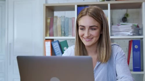 Woman works on laptop and drinks coffee at desk