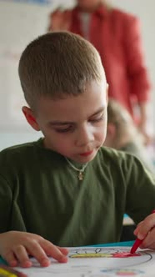 Young Boy Focused on Coloring and Drawing with a Red Marker at a Classroom Desk Engaging in Creative