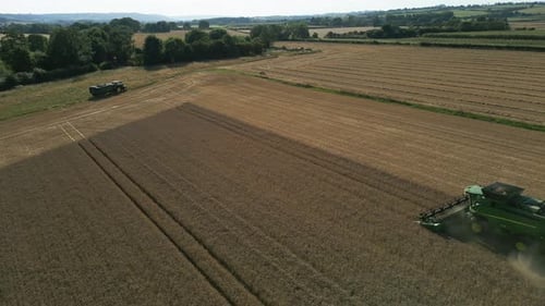 Pull Back Drone Shot of Green John Deere Combine Harvester Harvesting with lots of Dust and Tractor