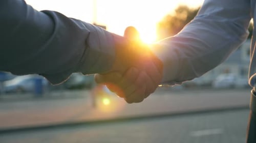 Close Up of Two Successful Businessmen Greeting Each Other Against the Background of Cars Parking