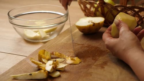 13 1Woman cutting peeled pear into slices on wooden board and placing pieces into a clear glass bowl