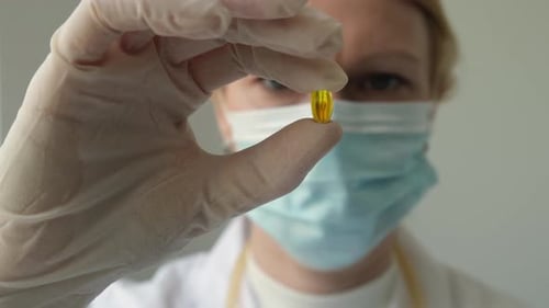 Close Up Hand of Female Doctor or Pharmacist in White Gloves Holding Yellow Omega 3 Capsule